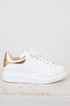 White sneaker with gold accents on a light background