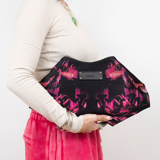 Person holding a black clutch with pink floral pattern against a white background