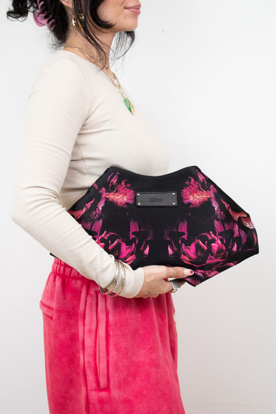 Person holding a black clutch with pink floral pattern against a white background