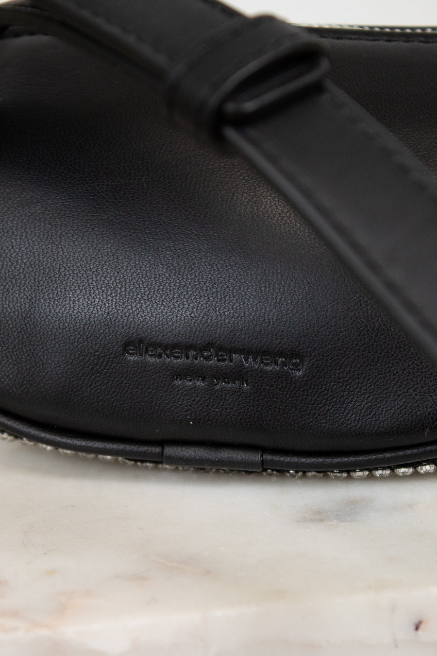 Black leather handbag on marble surface, featuring the Alexander Wang logo.