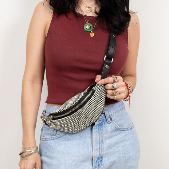 Woman wearing a maroon top and blue jeans with a beaded fanny pack against a plain background