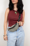 Woman wearing a maroon top and blue jeans with a beaded fanny pack against a plain background