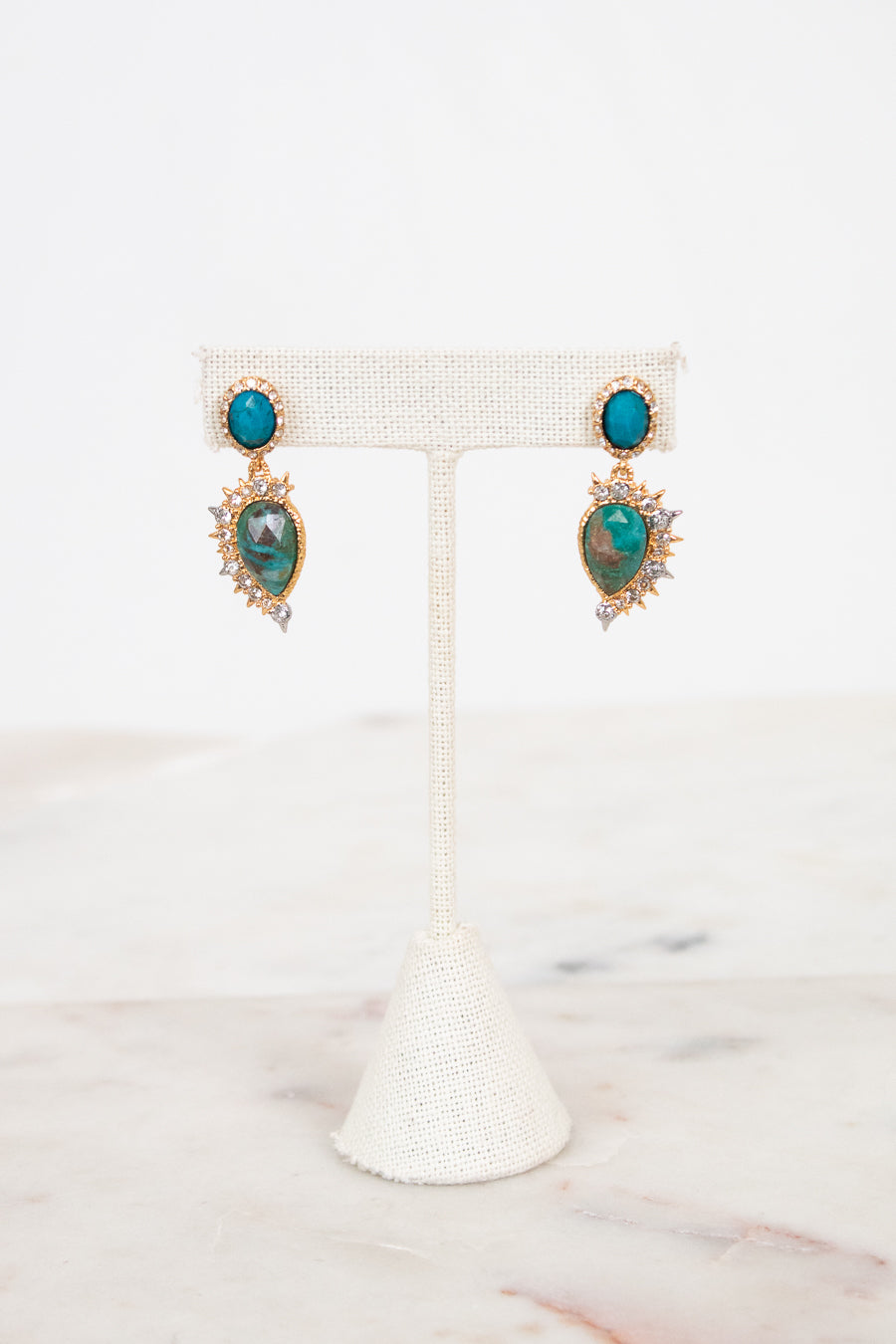 Pair of earrings with turquoise stones on a white stand against a marble background