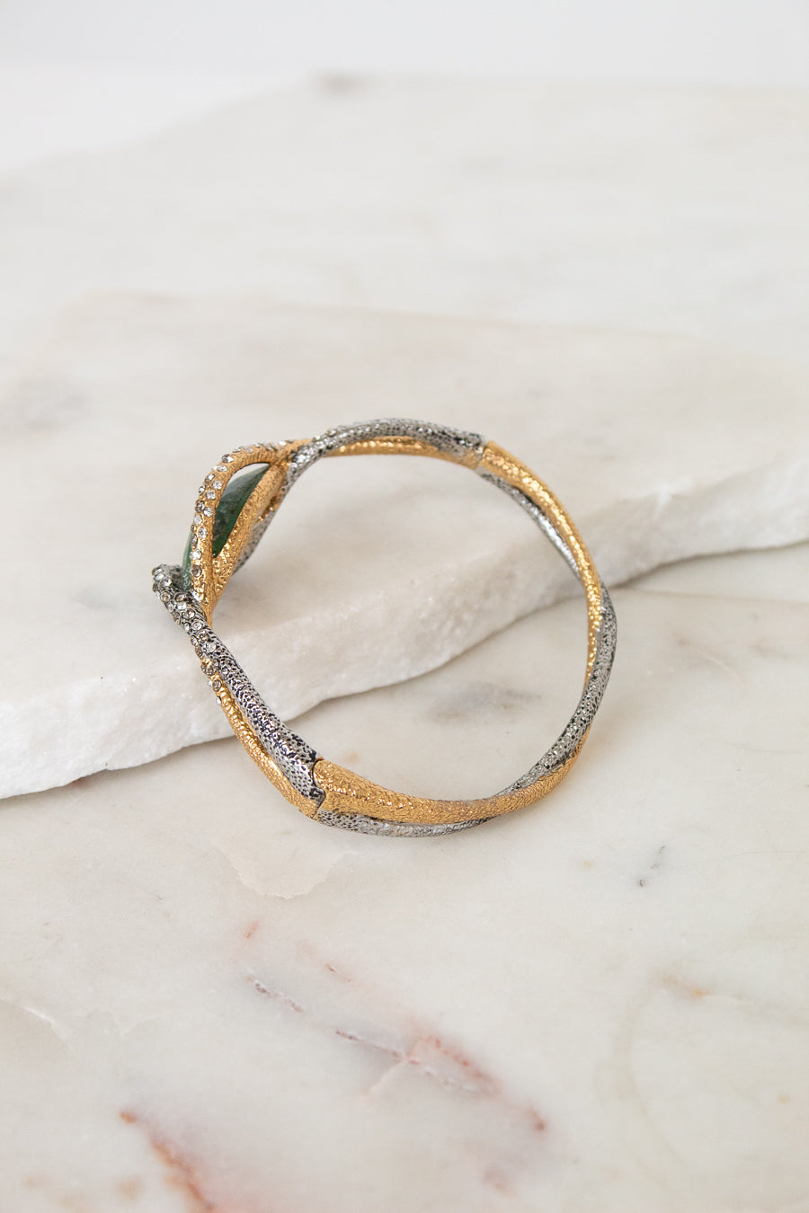 Gold and silver bracelet with twist detail on a marble surface