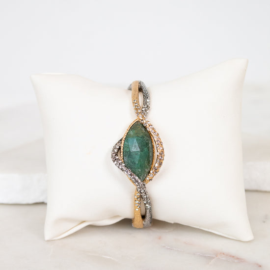 Bracelet with green stone center on a white cushion against a marble background