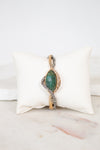 Bracelet with green stone center on a white cushion against a marble background
