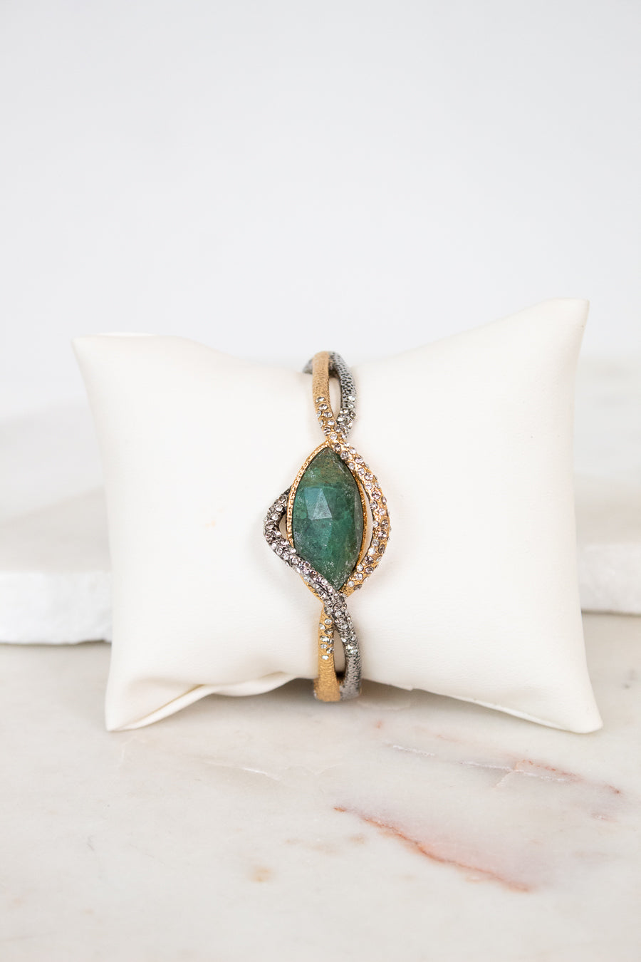 Bracelet with green stone center on a white cushion against a marble background