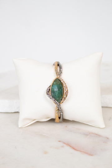 Bracelet with green stone center on a white cushion against a marble background