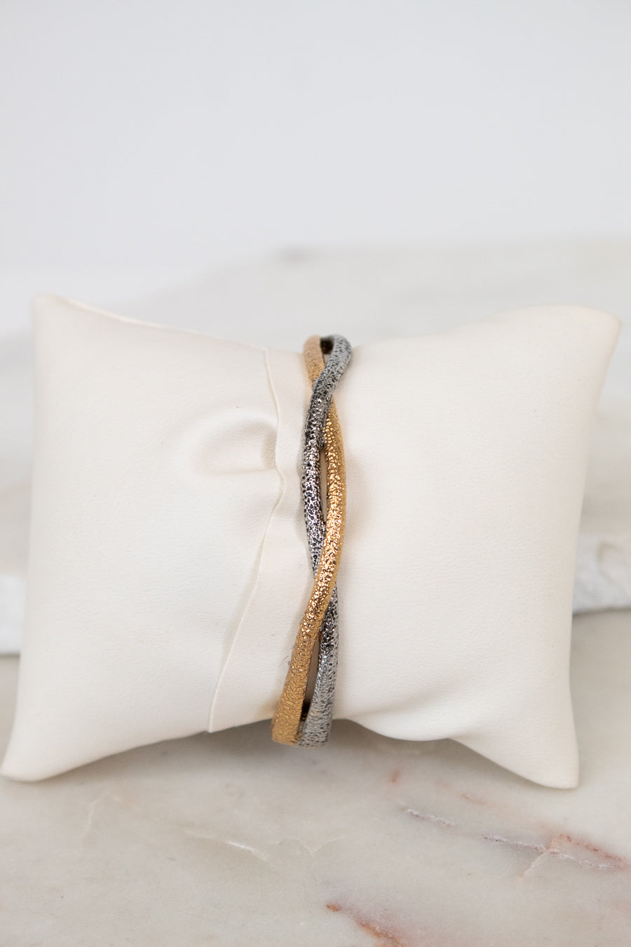 Two-tone bracelet on a white pillow with a marble surface