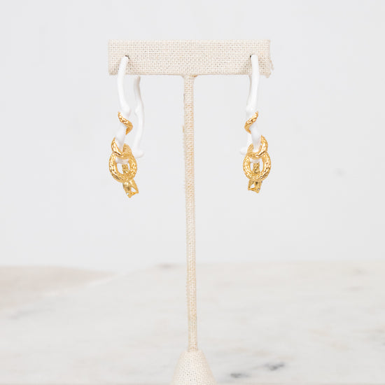 White earrings with gold details on a white stand with a white background