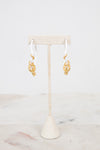 White earrings with gold details on a white stand with a white background