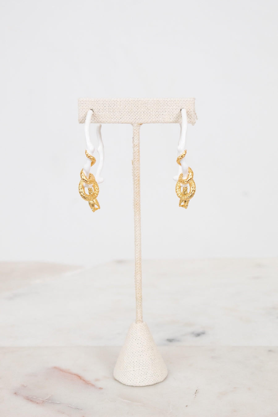 White earrings with gold details on a white stand with a white background