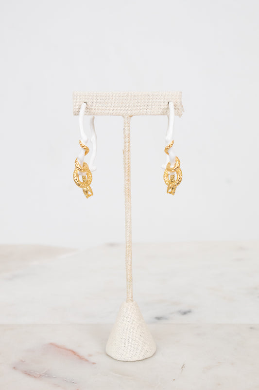 White earrings with gold details on a white stand with a white background