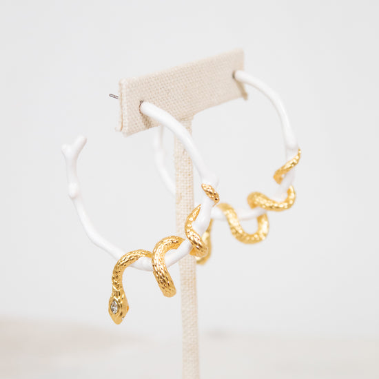 White hoop earrings with gold snake details on a white stand with a light beige background