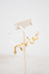 White hoop earrings with gold snake details on a white stand with a light beige background