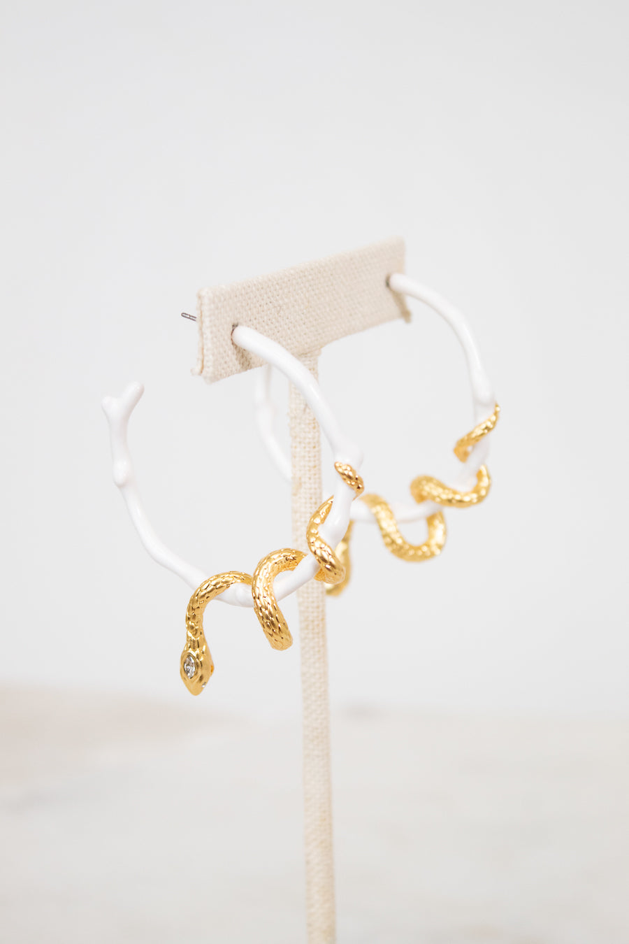 White hoop earrings with gold snake details on a white stand with a light beige background