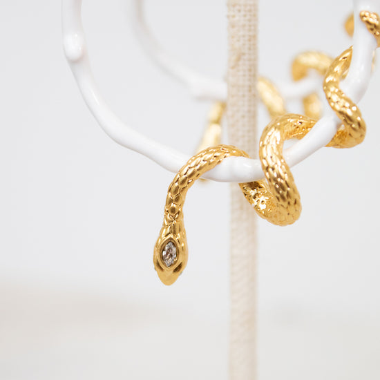 White hoop earring with gold snake details on a white stand with a white background