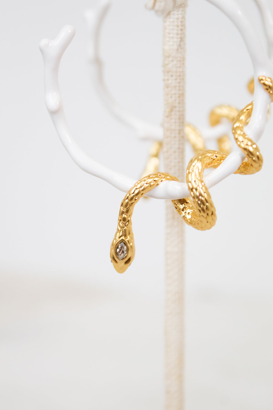 White hoop earring with gold snake details on a white stand with a white background