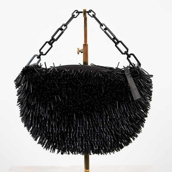 Black beaded handbag on a stand with a white background