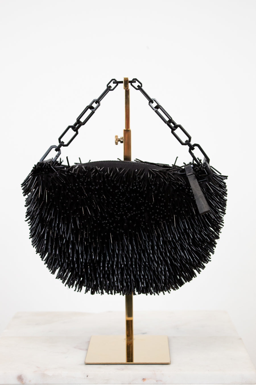 Black beaded handbag on a stand with a white background