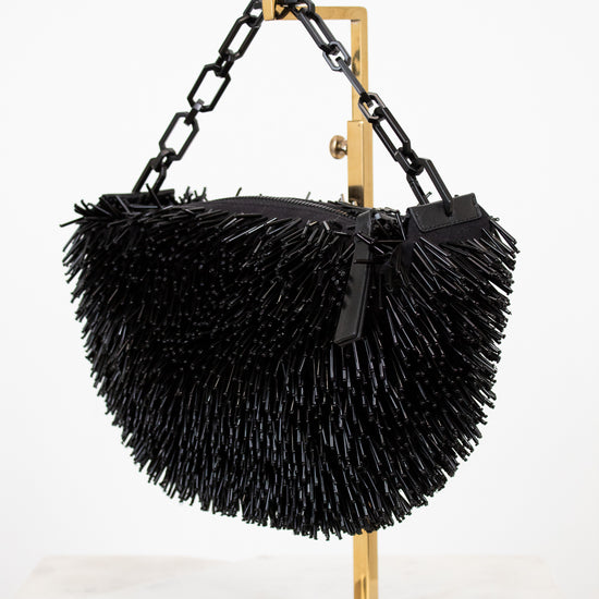 Black feathered handbag on a gold stand against a white background