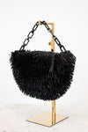 Black feathered handbag on a gold stand against a white background