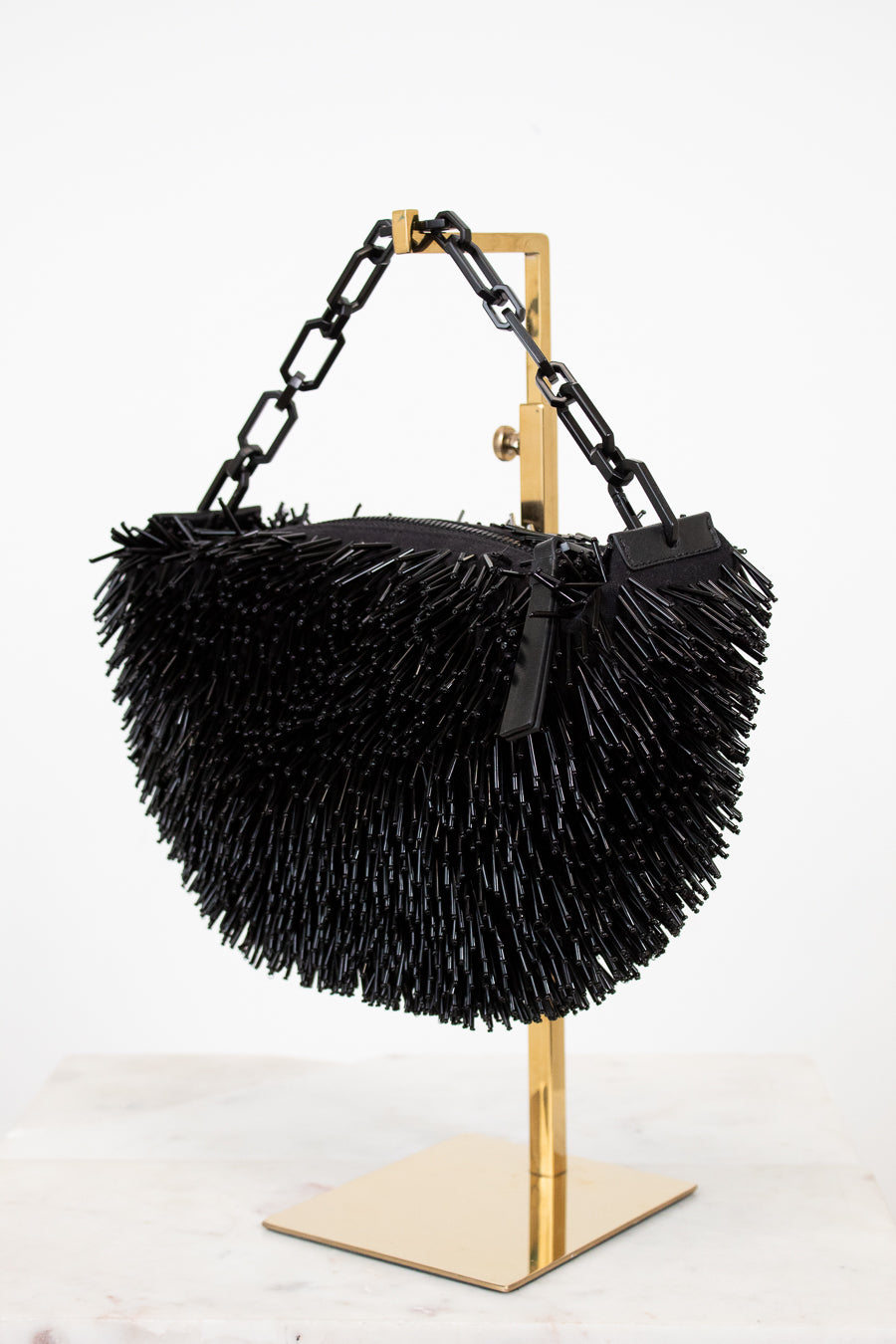 Black feathered handbag on a gold stand against a white background