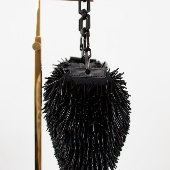 Black beaded purse on a chain with a metal handle against a white background