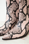 Close-up of pointed-toe ankle boots with a pink, black, and beige snakeskin pattern on a light marble surface.