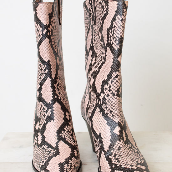 A pair of pointed-toe mid-calf boots featuring a pink and black snakeskin pattern, set against a clean white background.