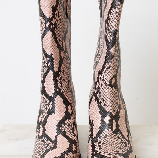 A pair of pointed-toe ankle boots featuring a pink and black snakeskin pattern, displayed against a clean white background.