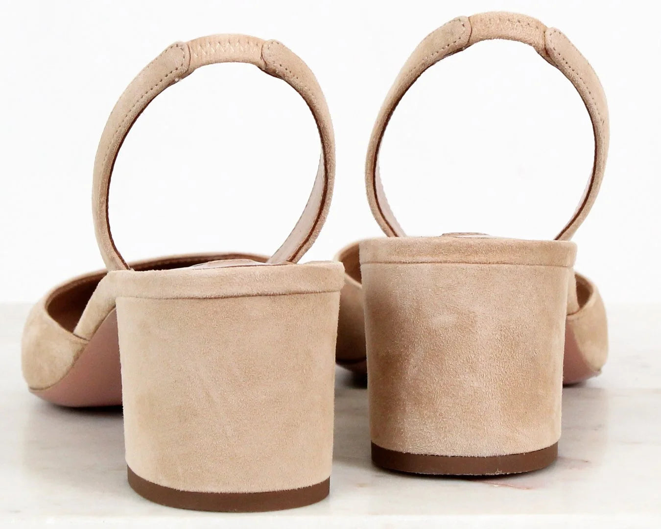 Pair of beige suede shoes with circular handles on a white background