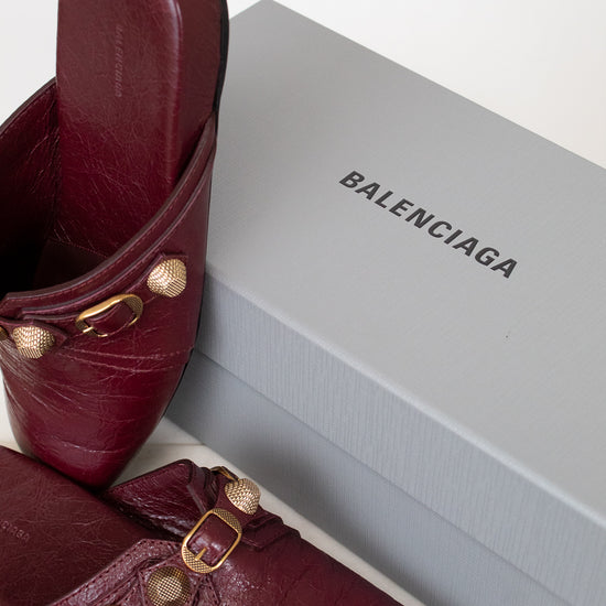 Burgundy mules with gold hardware set against a gray 'Balenciaga' branded box