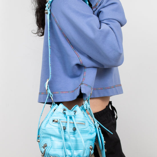 Person wearing a blue jacket and holding a matching blue bag against a white background