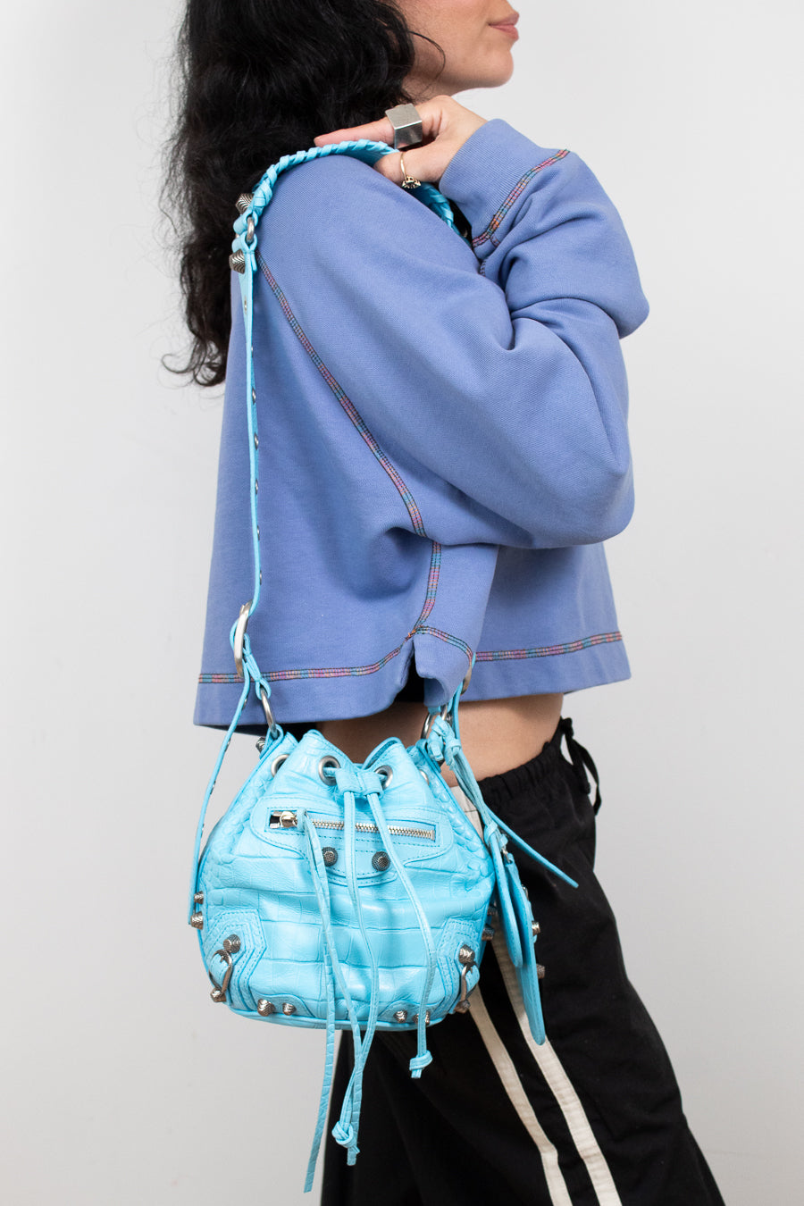 Person wearing a blue jacket and holding a matching blue bag against a white background