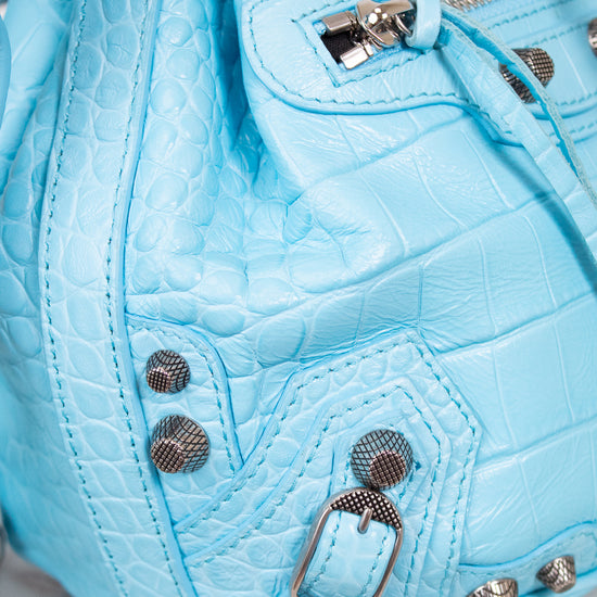 Close-up of a light blue textured handbag with metallic accents on a marble surface.