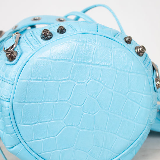 Light blue crocodile-embossed leather handbag with decorative elements on a white background