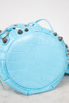 Light blue crocodile-embossed leather handbag with decorative elements on a white background