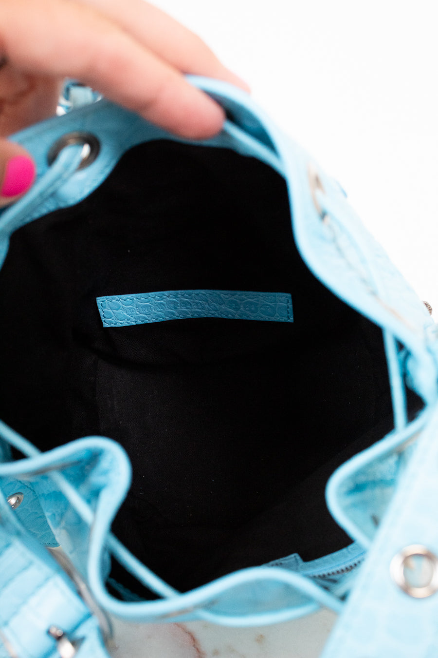 Close-up of a light blue interior of handbag with a hand holding it open, showing the interior.