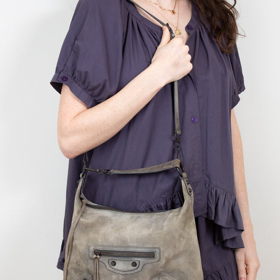 Woman wearing a purple blouse holding a gray shoulder bag against a white background