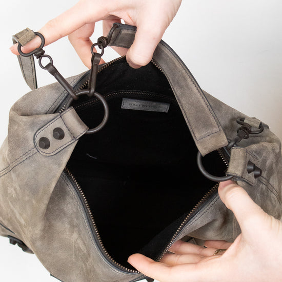 Gray shoulder bag being held open by a person's hands on a light gray background