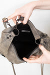 Gray shoulder bag being held open by a person's hands on a light gray background