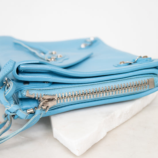 Light blue leather handbag with zippers on a white marble surface