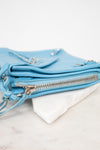 Light blue leather handbag with zippers on a white marble surface