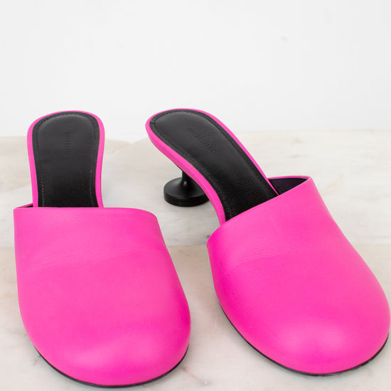 Pair of bright pink mules with black interiors on a light marble background