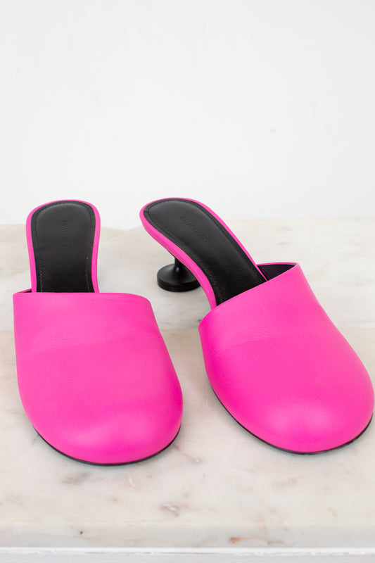 Pair of bright pink mules with black interiors on a light marble background