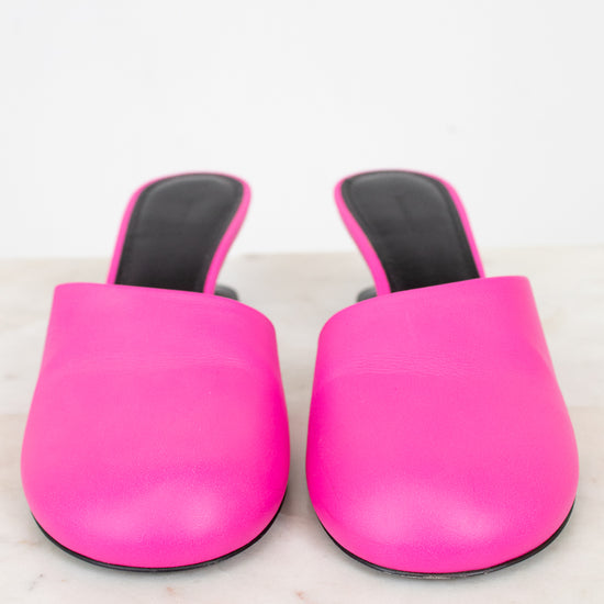Pair of bright pink slip on high heel with black soles on a light marble background