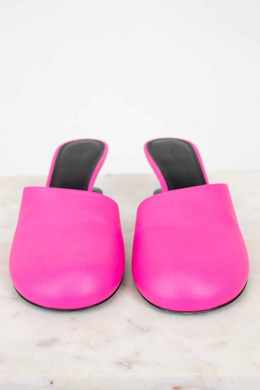 Pair of bright pink slip on high heel with black soles on a light marble background