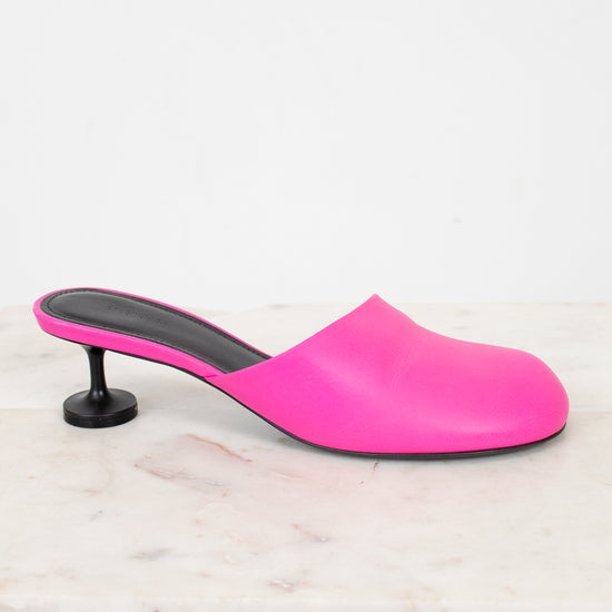 Pink high-heeled slip on heel sitting on a light marble background