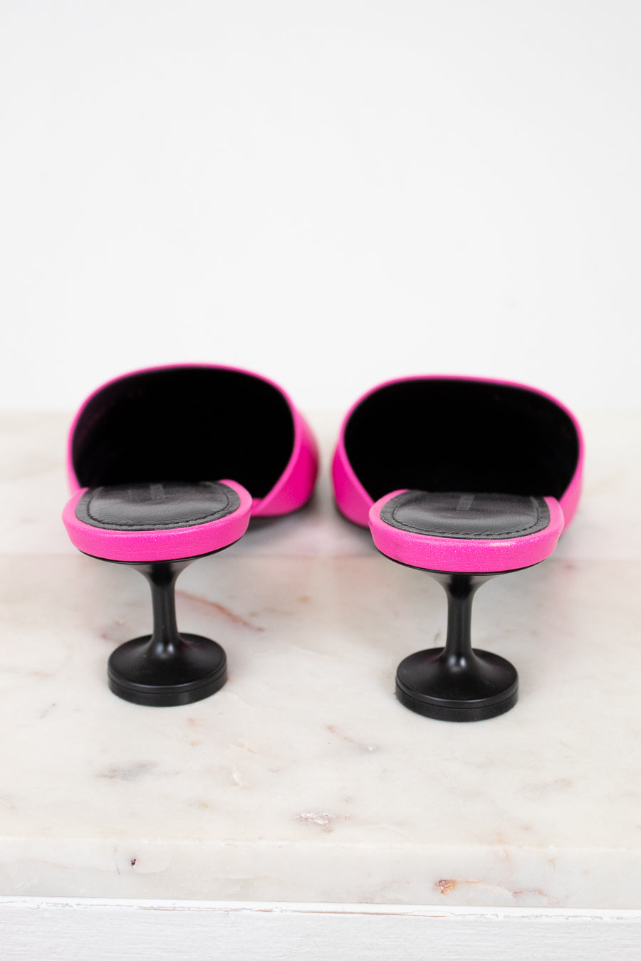 Pair of pink and black high heeled shoes on a marble surface with a white background